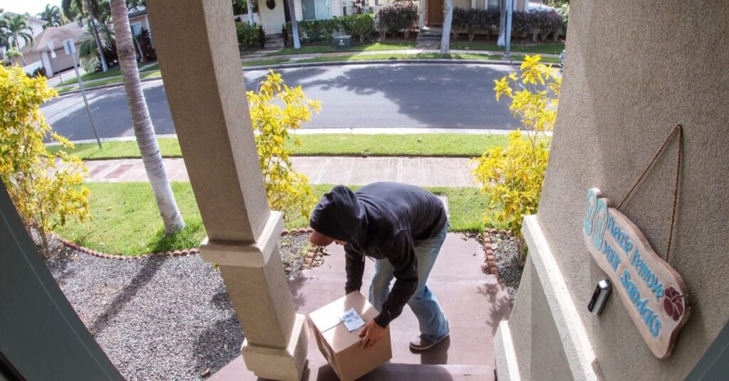 Man stealing a package off of a porch.