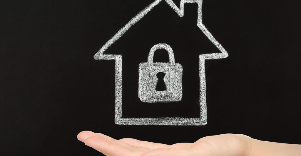 Chalk drawing of a home with a padlock in the middle in the palm of a hand.