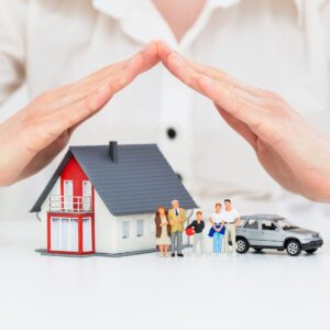 a person with their hands over a toy house, family, and car, protecting them